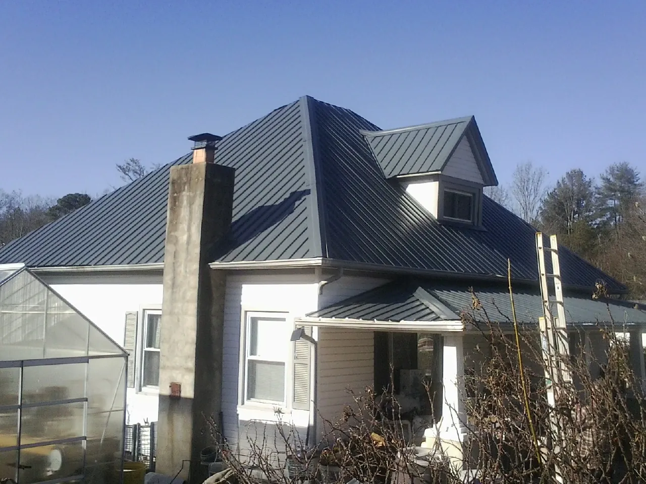 Dark blue standing seam metal roof on a white farmhouse with dormer — Slate & Tile Roof Repair by Roofing Brothers in East Galesburg