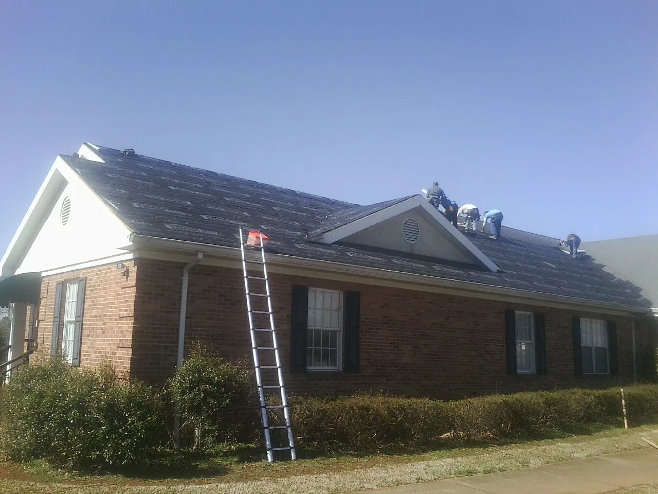 Crew tearing shingles off a brick ranch roof with a ladder set — Emergency Roof Repair work by our crew in East Galesburg