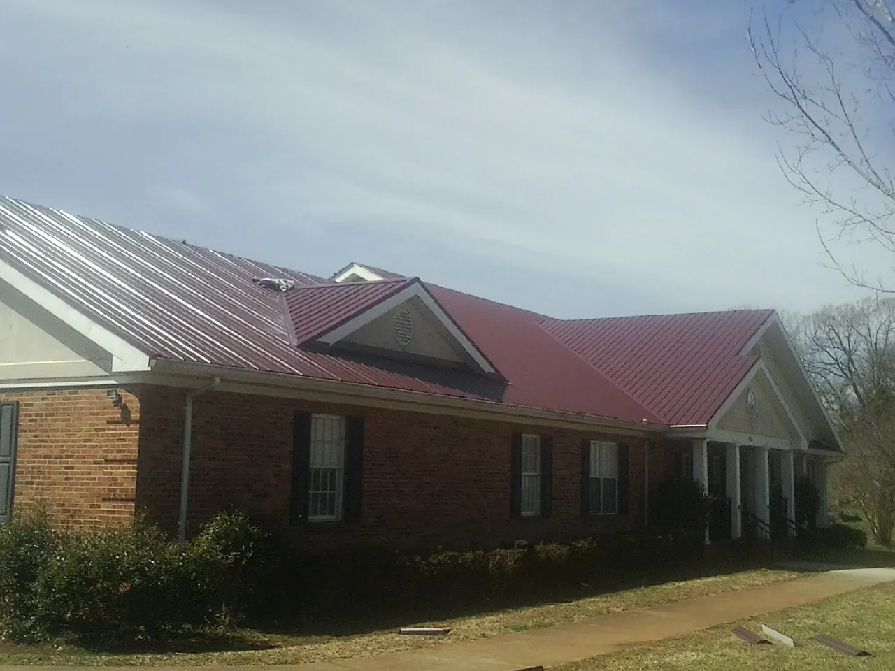 Red metal roof with gabled entries on a long brick building, from a Hail Damage Roof Repair job in East Galesburg
