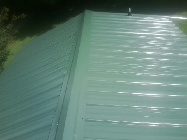 New green metal panels meeting at the ridge of a roof — Flat Roof Repair work by our crew in East Galesburg
