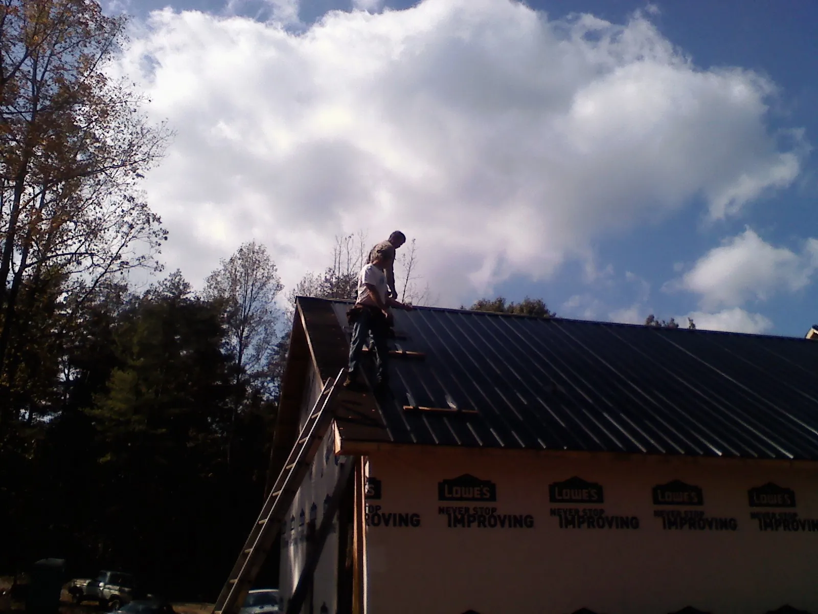 Roofer fastening dark metal panels high against a cloudy sky, from a Roof Inspection job in East Galesburg