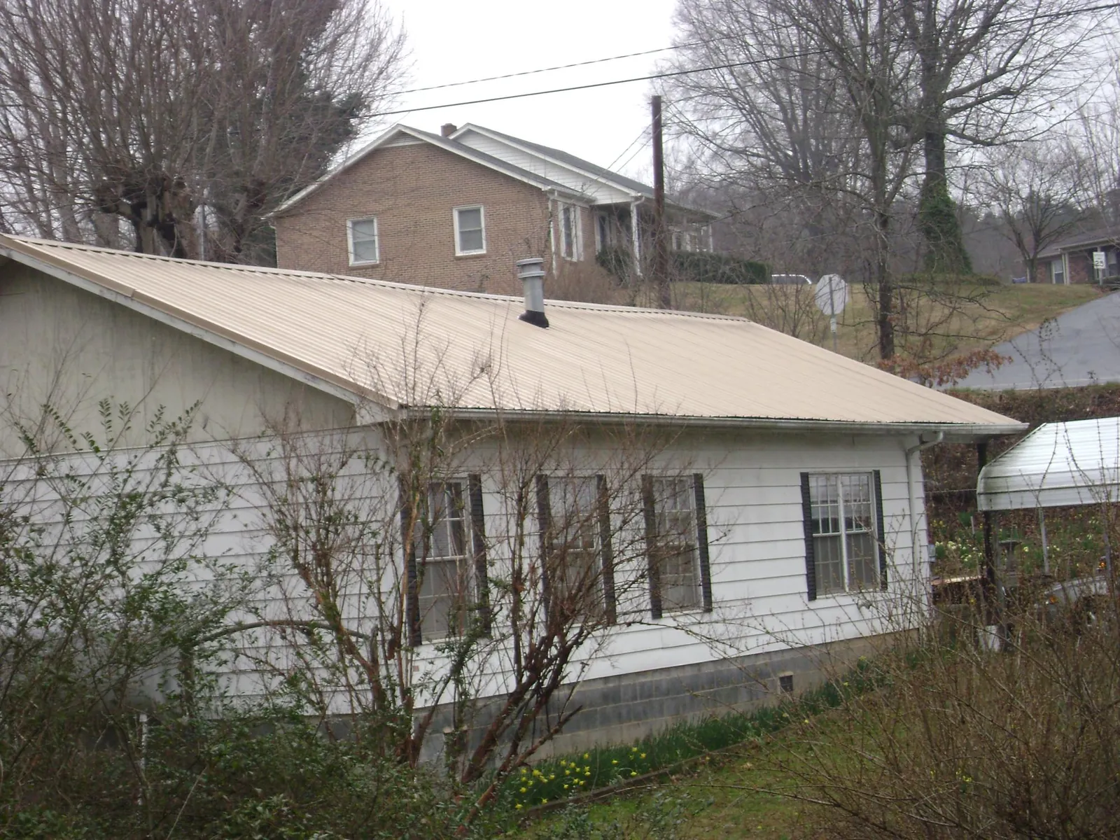 Tan metal roof on a white sided house set into a hillside — Commercial Roofing by Roofing Brothers in East Galesburg